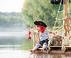 Ein Kind in Piratenkostüm sitzt auf einem Floß mit Steuerrad