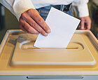 Eine Hand steckt einen Zettel in eine Wahlurne